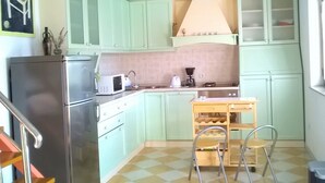 Una cocina compacta con armarios verdes, un refrigerador, un microondas, una cafetera y una pequeña mesa de comedor con sillas.