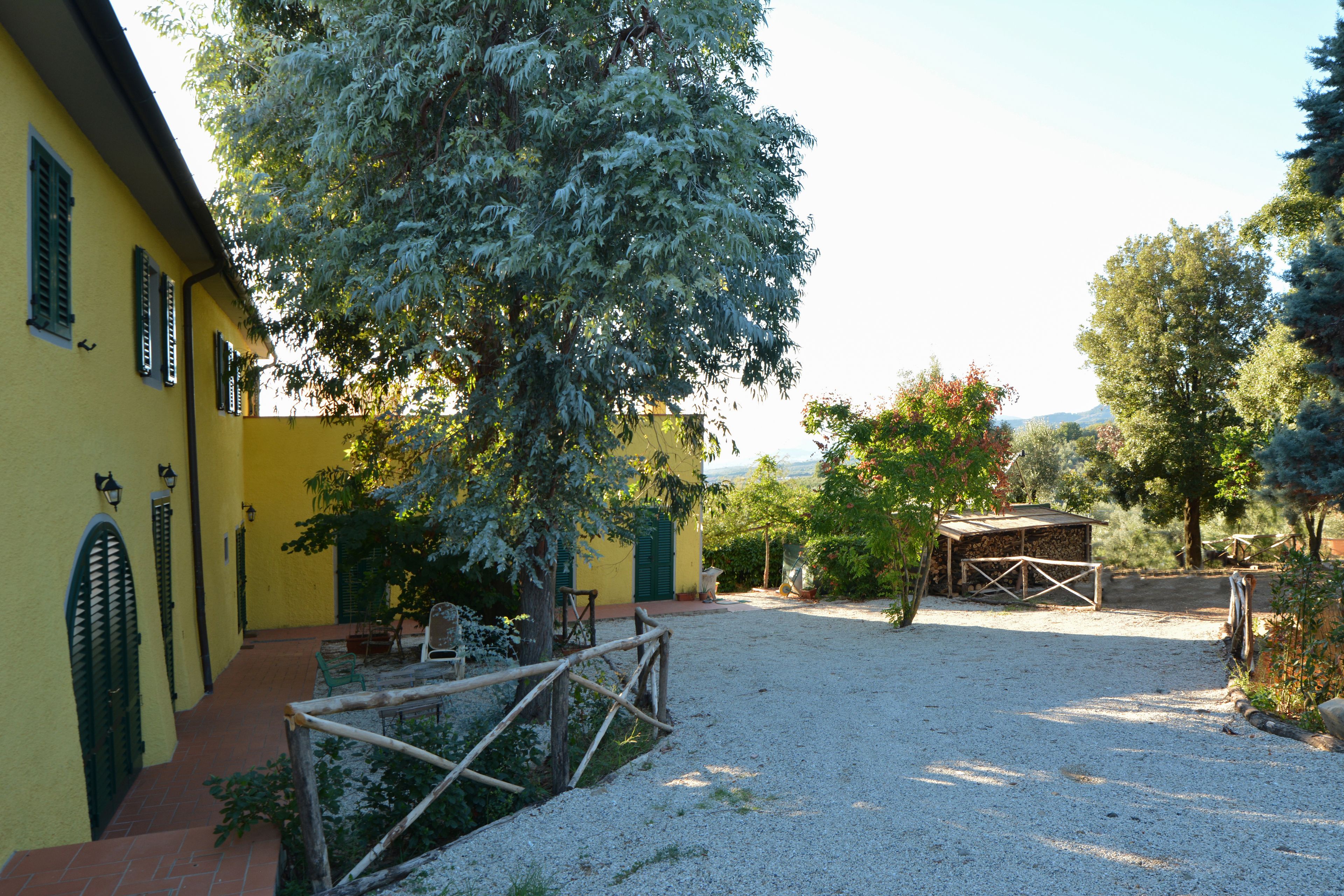 A courtyard with a yellow building, a wooden fence, and a gravel path.