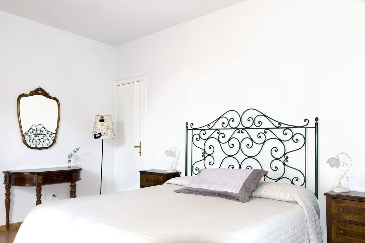 A bedroom with a bed, a dresser, a nightstand, a mirror, and a lamp.