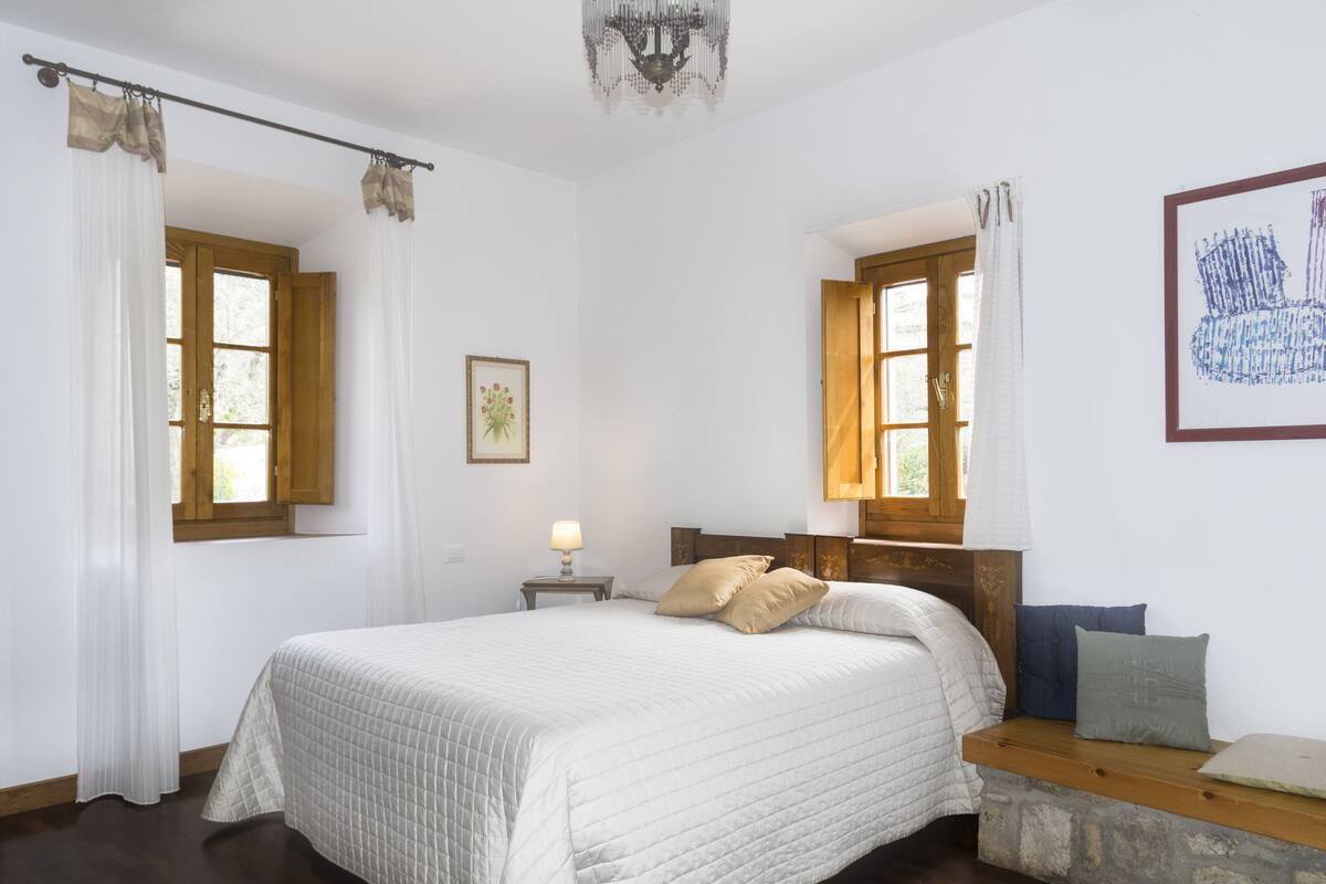 A bedroom with a bed, a nightstand, a lamp, a window with curtains, and a framed picture on the wall.