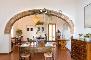 A dining area with a brick archway, wooden table, chairs, and a chandelier.