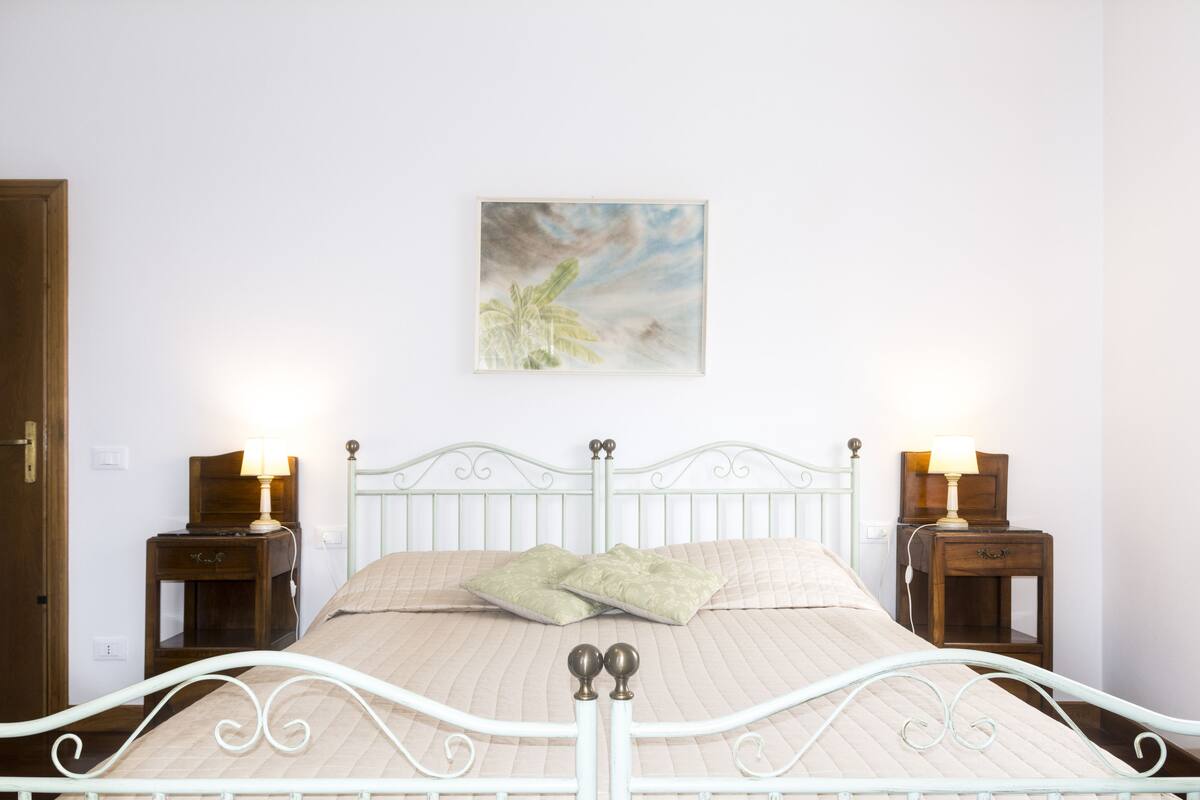 A neatly made bed with a headboard, two bedside tables with lamps, and a painting on the wall.