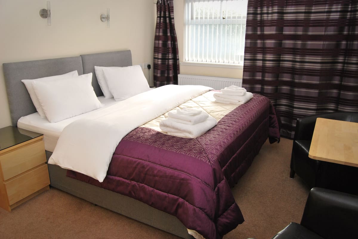 A hotel room with a bed, bedside table, chair, and window with curtains.