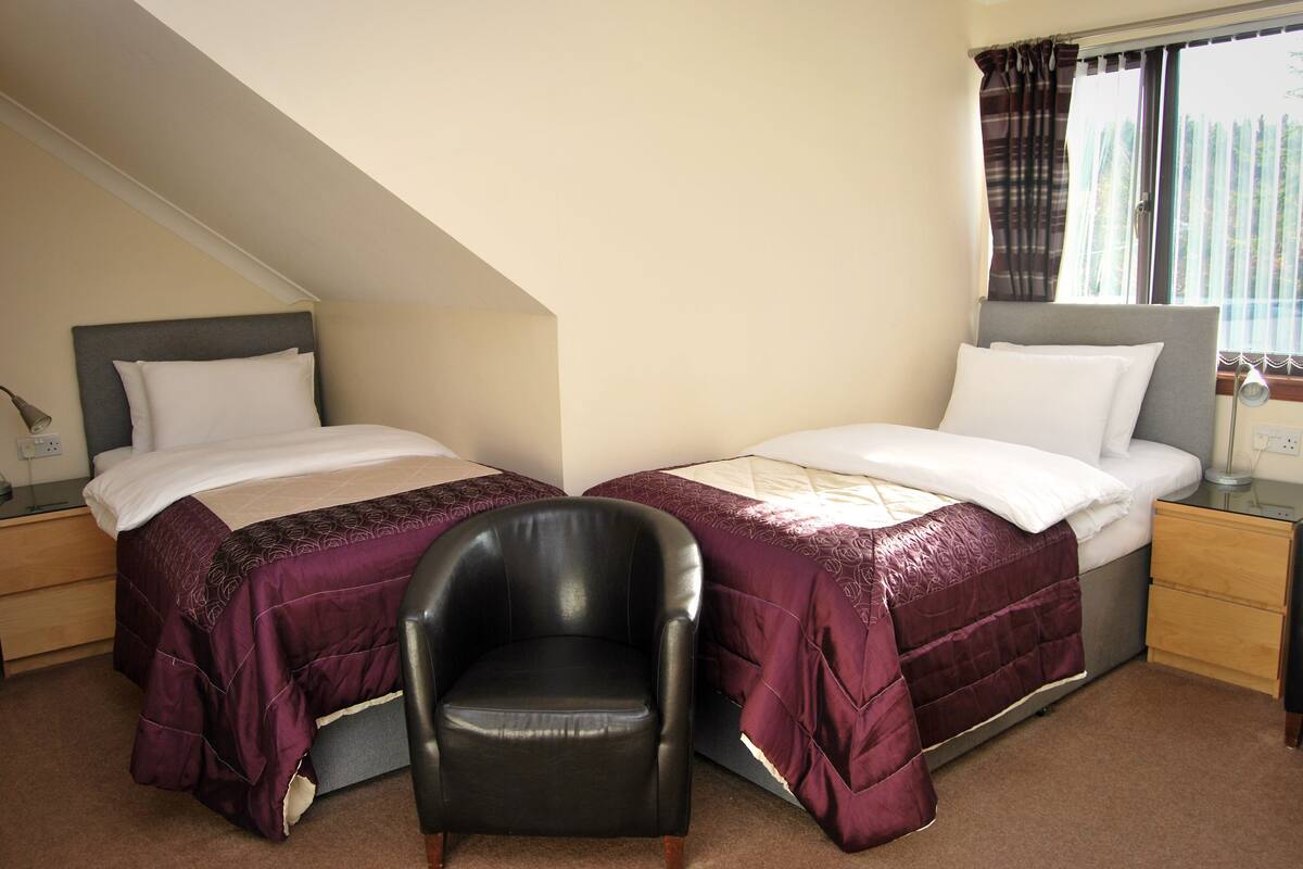 A twin room with two beds, a chair, and a window with curtains.