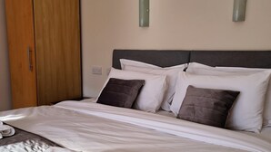 A neatly made bed with white linens and two pillows, a wooden wardrobe, and two wall-mounted light fixtures. - The Old Schoolhouse Hotel (Larkhall)