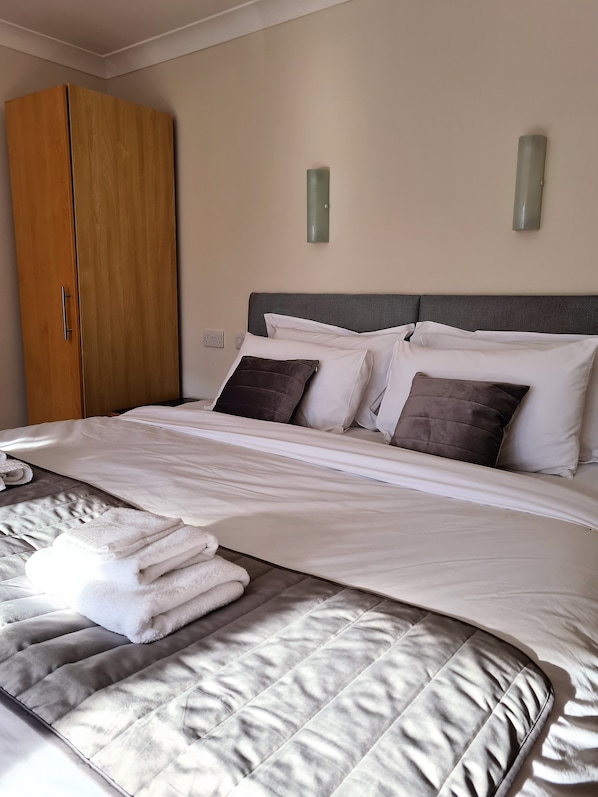 A neatly made bed with white linens and two pillows, a wooden wardrobe, and two wall-mounted light fixtures.