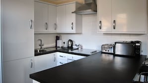 A modern kitchen with white cabinets, a black countertop, a stainless steel toaster, and a kettle. - The Old Schoolhouse Hotel (Larkhall)