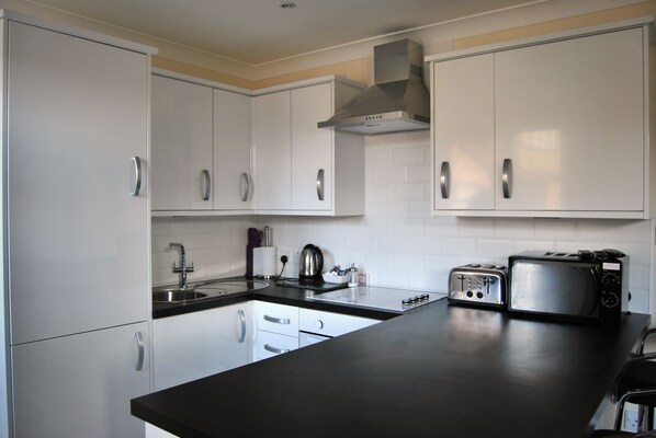 A modern kitchen with white cabinets, a black countertop, a stainless steel toaster, and a kettle. - The Old Schoolhouse Hotel (Larkhall)