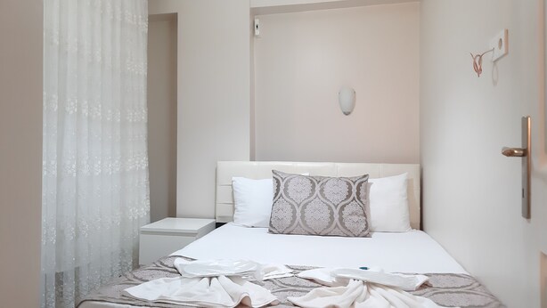 A neatly made bed with a patterned pillow, a bedside table, and a wall-mounted light fixture. - Burak Apart Otel (Istanbul)