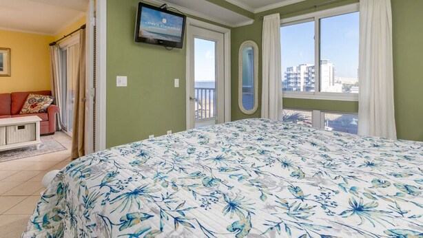 Une chambre dotée d’un grand lit, d’un ventilateur de plafond, d’un téléviseur fixé au mur et d’un balcon offrant une vue sur la ville.