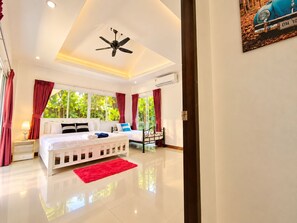 A hotel room with a bed, a red rug, a ceiling fan, and a window with curtains. - Chalong 4BR Private Pool Villa | Near Big Buddha | Sleeps 10 (Tambon Chalong)