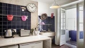 Una cucina con zoccolo a mosaico nero, piano di lavoro bianco, bollitore, tostapane, lavello e lampada a sospensione.