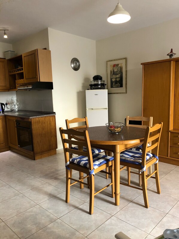 A kitchen with wooden cabinets, a dining table with chairs, a refrigerator, and a clock on the wall.