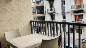 A balcony with a table and two chairs, overlooking a street with parked cars and a building with multiple balconies. - Private Apartment... (FREE WIFI ) (st pauls bay)