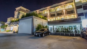 A modern building with multiple floors, a parking area, and a black car parked in front. - A Nice clean superior king or twin room (Tambon Wichit)