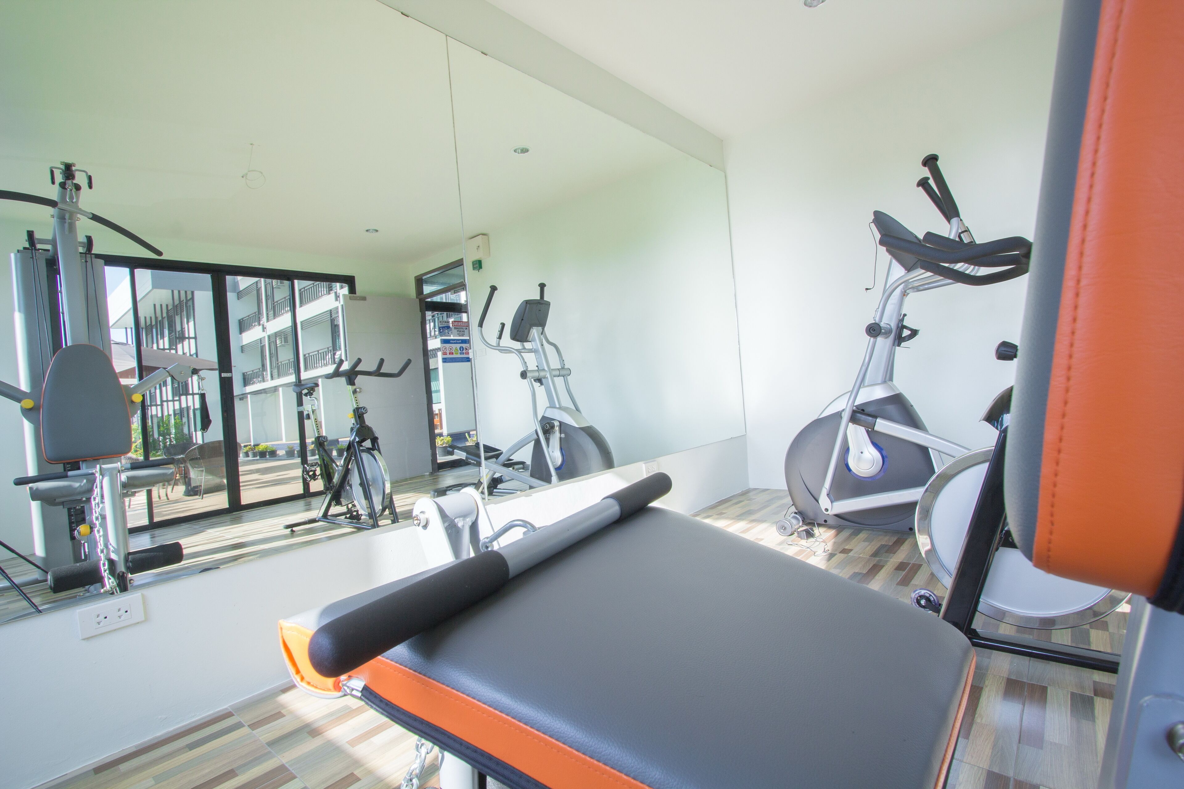 A gym with exercise equipment, a mirror, and a wooden floor.