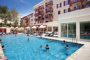 Ein Schwimmbecken mit mehreren Balkonebenen, Liegestühlen und Sonnenschirmen.
