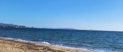 A beach with a clear sky, calm sea, and distant landforms.
