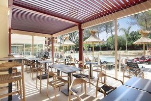 An outdoor seating area with tables and chairs, a pool, and umbrellas.