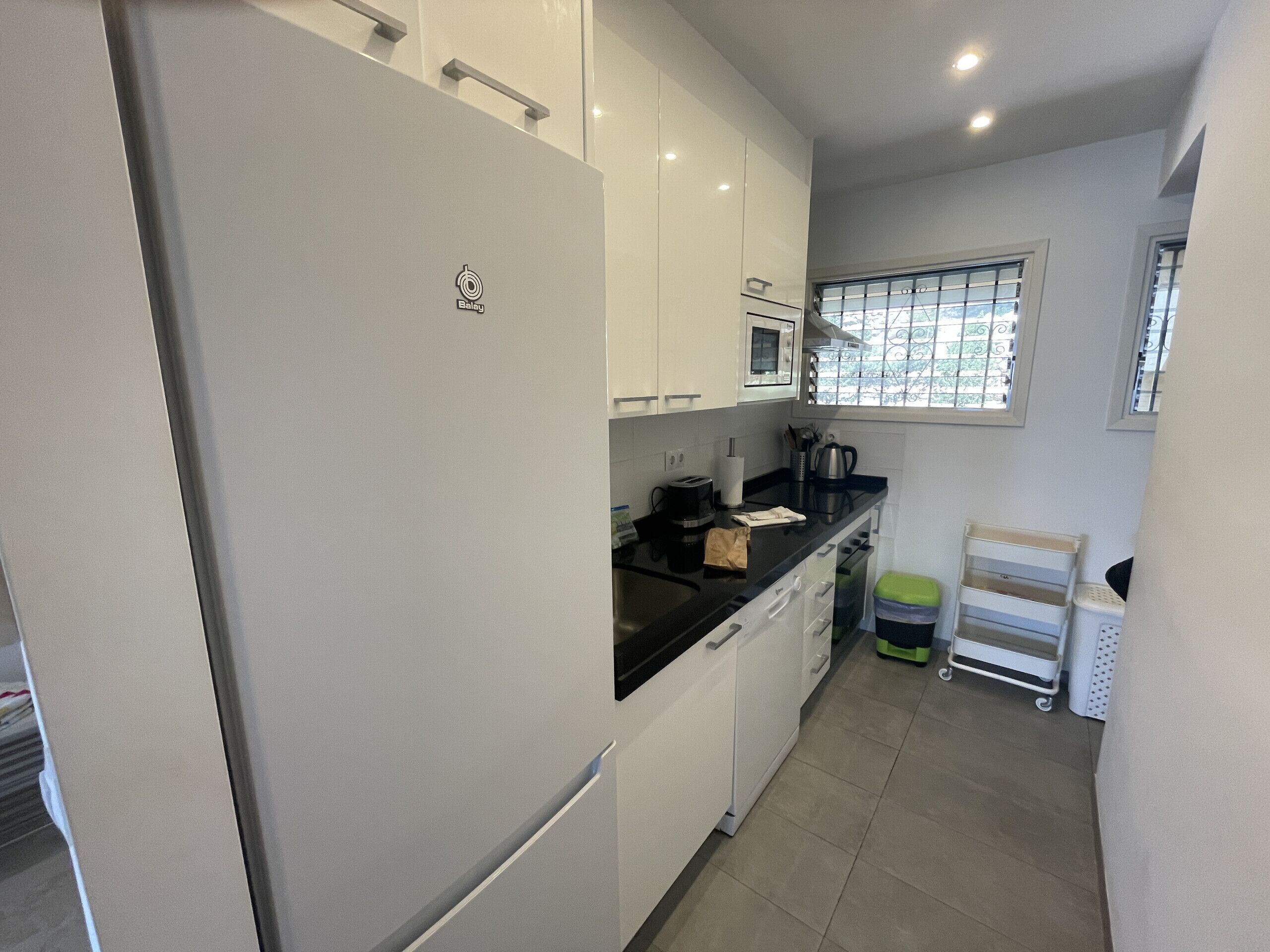 Una cocina compacta con armarios blancos, encimera negra y refrigerador de acero inoxidable.