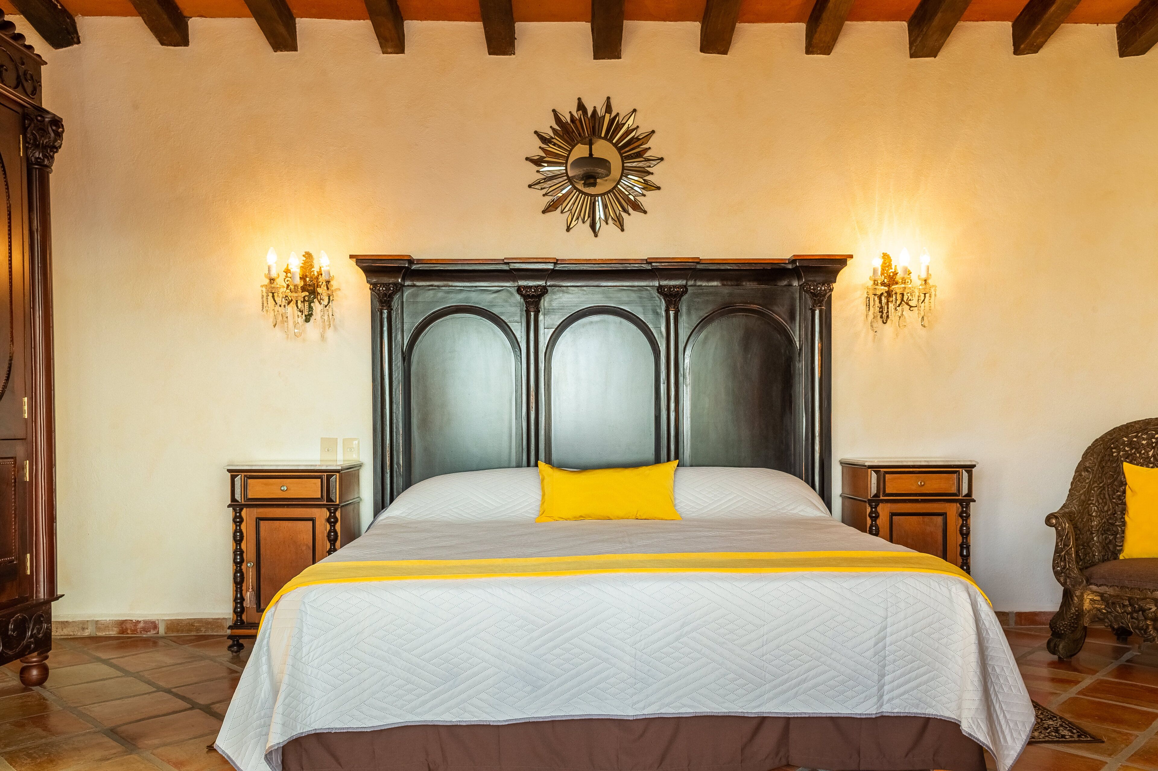 A bedroom with a large bed, two nightstands, a chandelier, and a decorative wall piece.