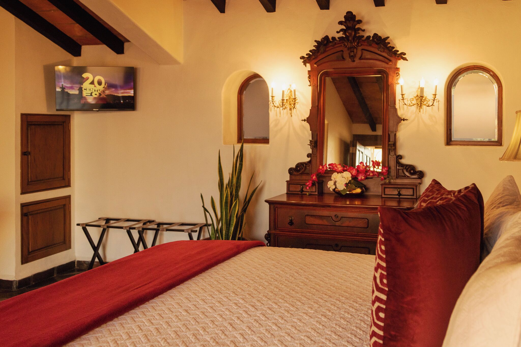 Ein Hotelzimmer mit Bett, Schminktisch, Spiegel, Fernseher und einer Kristallleuchtre.