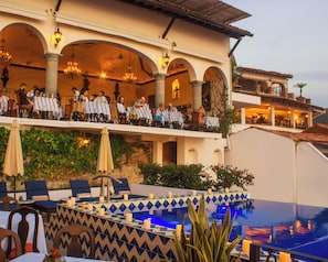 A hotel with outdoor seating, a pool, and a dining area with guests.