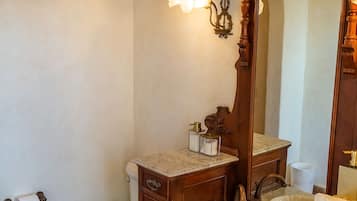 Casa de banho com sanita branca, toucador de madeira com lavatório e um espelho grande.