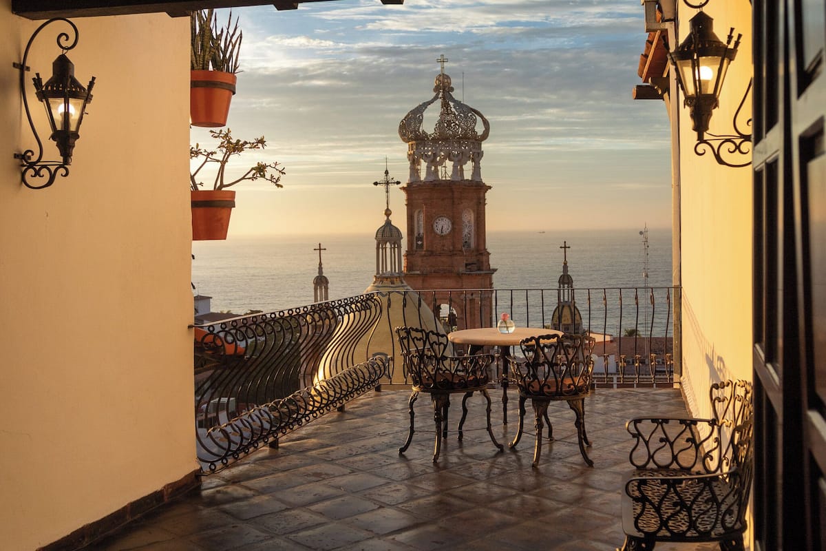A balcony with a view of the sea, a clock tower, and a table with chairs.