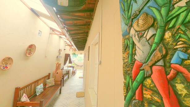 Un pasillo estrecho con un mural en la pared derecha, un banco a la izquierda y una puerta al final.