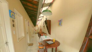 Un pasillo estrecho con una zona de comedor que incluye una mesa de madera y taburetes, una lámpara verde colgante y un piso de baldosas.