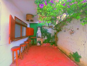 A narrow outdoor area with a brick wall, a small tree with purple flowers, a chimney, and a red floor. - Casa da Pituba (Itacaré)