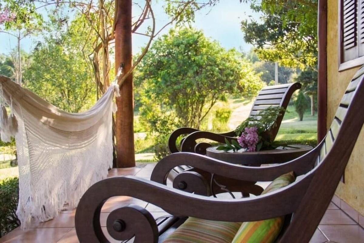 Una hamaca y dos sillas de madera en un patio con vista a un jardín.