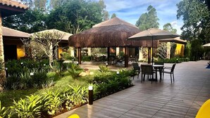Un patio con mobiliario exterior, estructuras de techo de paja y abundante vegetación.