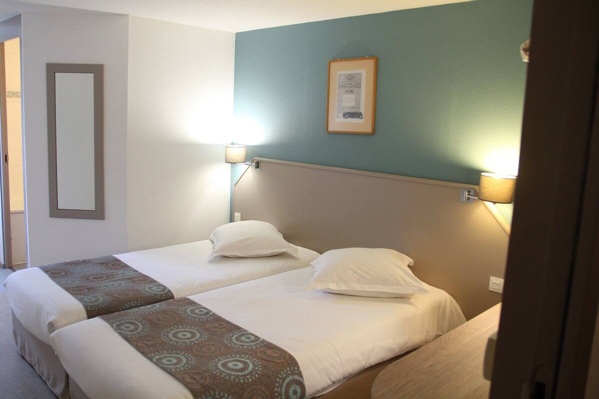 Une chambre d’hôtel avec deux lits, un tableau encadré au mur et deux lampes fixées au mur.