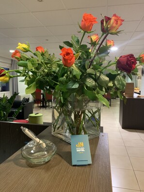 A bouquet of roses in a glass vase on a wooden table with a sign for Doues Hotel. - Doubs Hotel - Hostel (Ecole-Valentin)