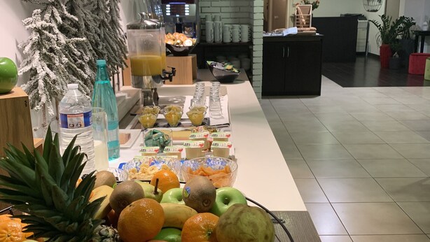 A breakfast buffet with fruits and beverages, a coffee machine, and a brick wall in the background. - Doubs Hotel - Hostel (Ecole-Valentin)