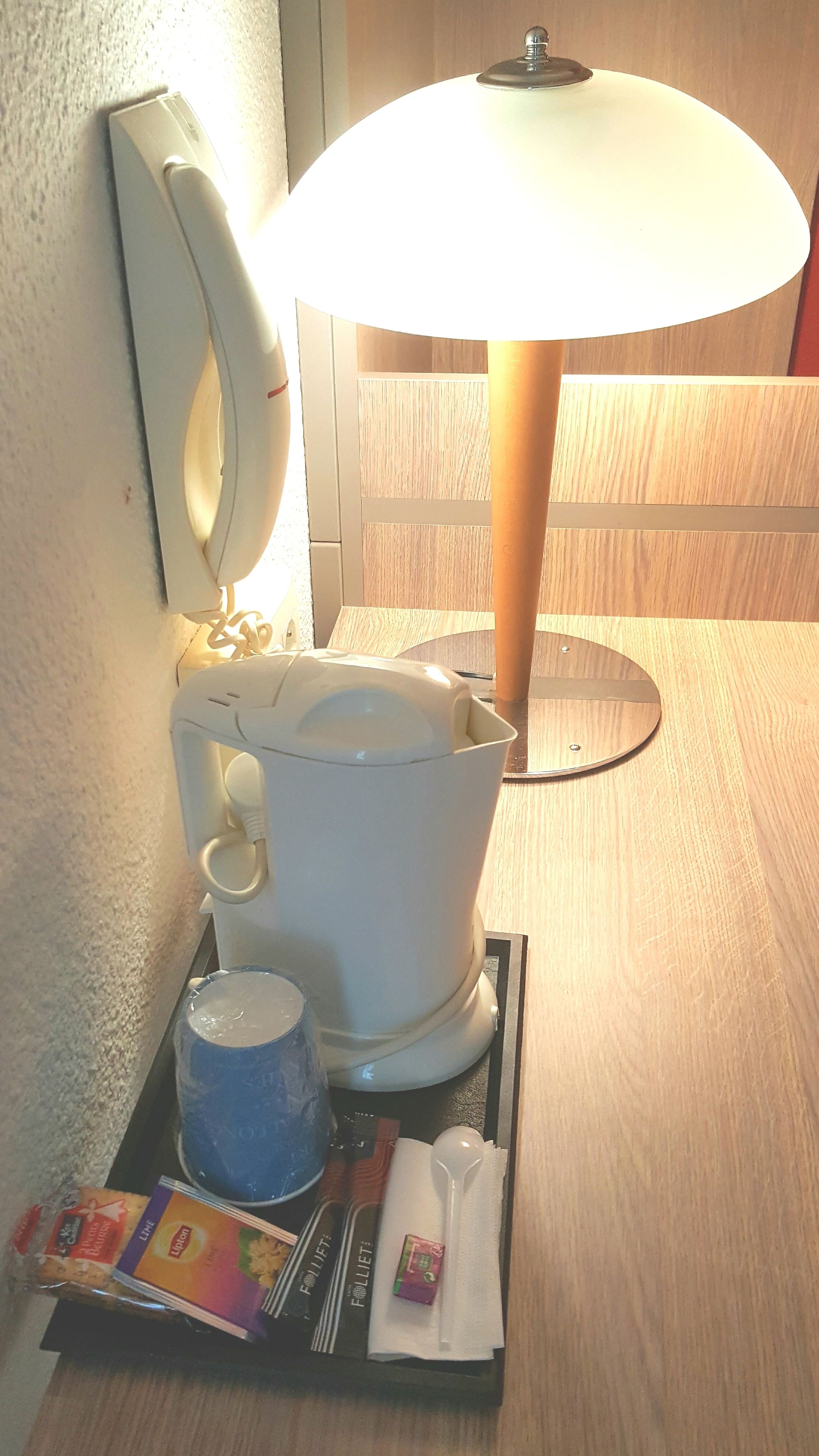 A bathroom with a white toilet, a white sink, and a white lamp. There are toiletries on the tray.