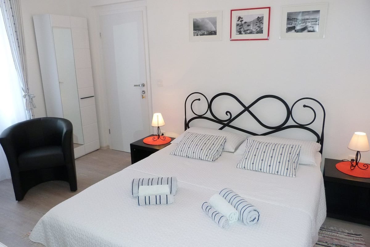A neatly arranged bedroom with a bed, two nightstands, a chair, and framed pictures on the wall.