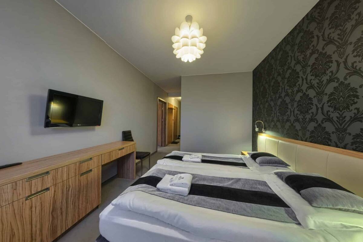 A hotel room with two beds, a TV, a desk, and a chandelier.
