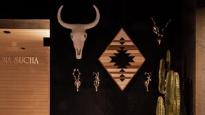 A room with a leather chair, a cactus plant, a wall with a bull skull and geometric patterns, and a sign reading 'UNA SUCHA'.
