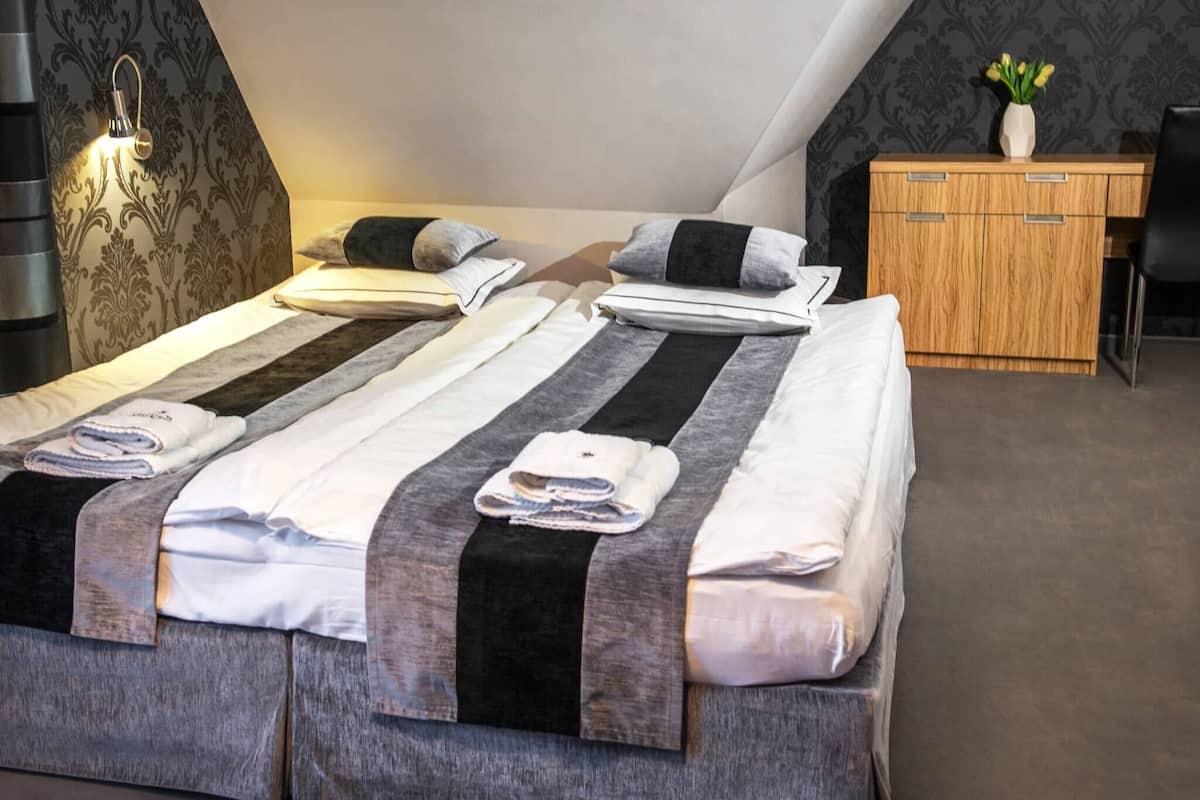 A neatly made bed with striped bedding and towels, a bedside lamp, and a wooden cabinet with a vase of flowers.