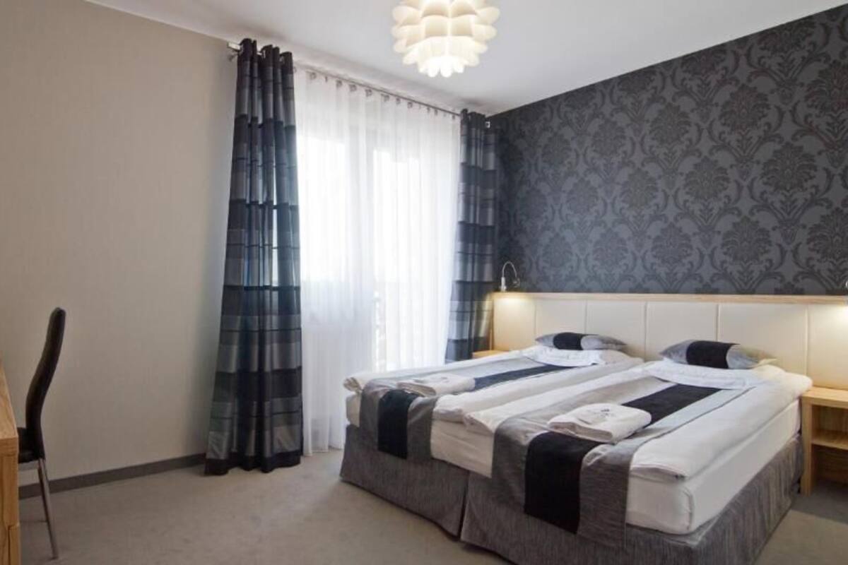 A hotel room with a bed, bedside tables, a desk, a chair, a TV, and a curtain.