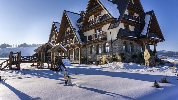 A large, multi-story chalet with a stone facade and wooden balconies, surrounded by snow.