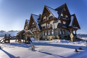 Een groot, meerlaags chalet met een gevel van natuursteen en houten balkons, omringd door sneeuw.