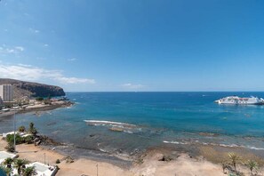 A coastal view with a cruise ship, rocky shoreline, and buildings in the background.