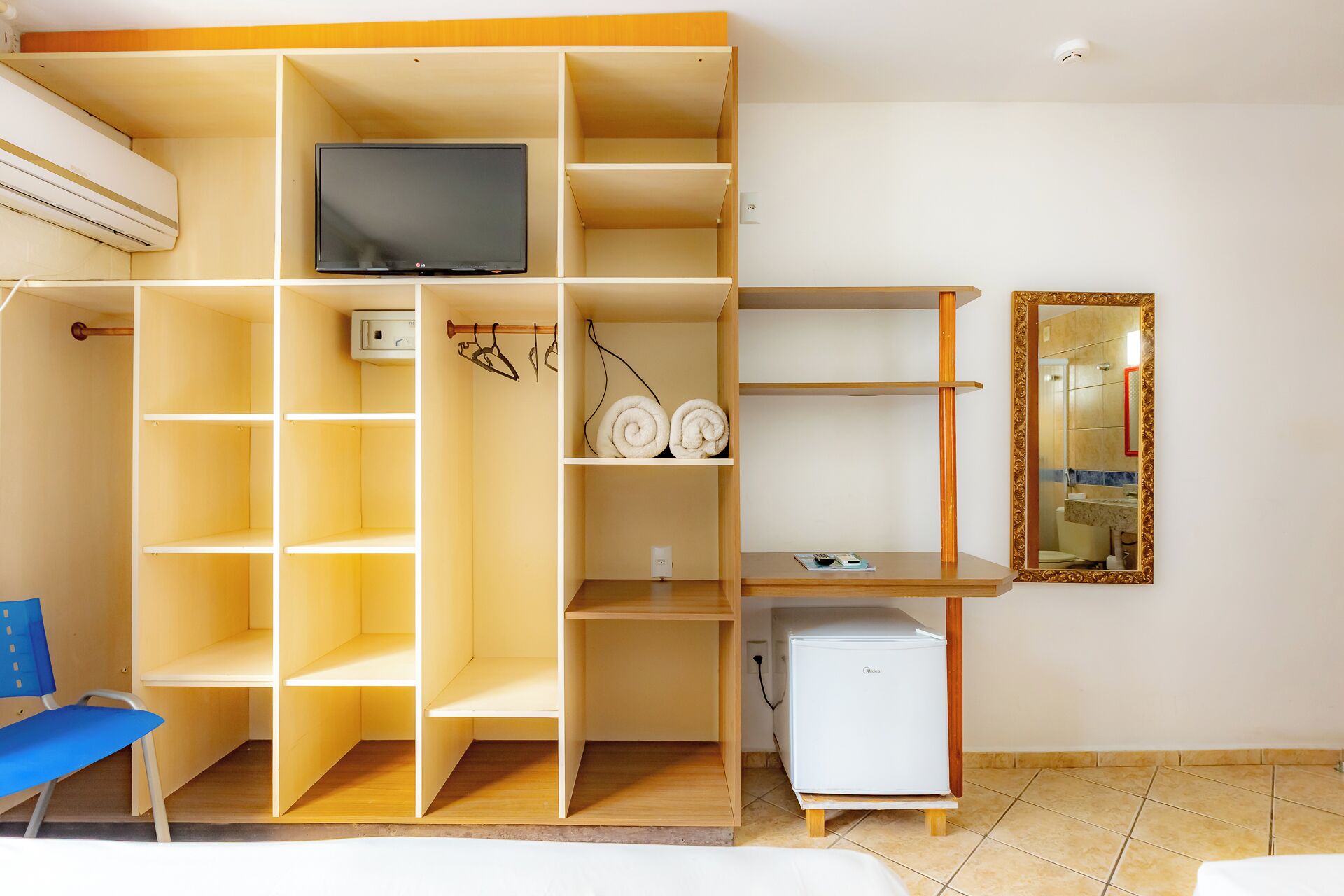 Een kamer met een televisie, een kleine koelkast, een spiegel en een stoel.