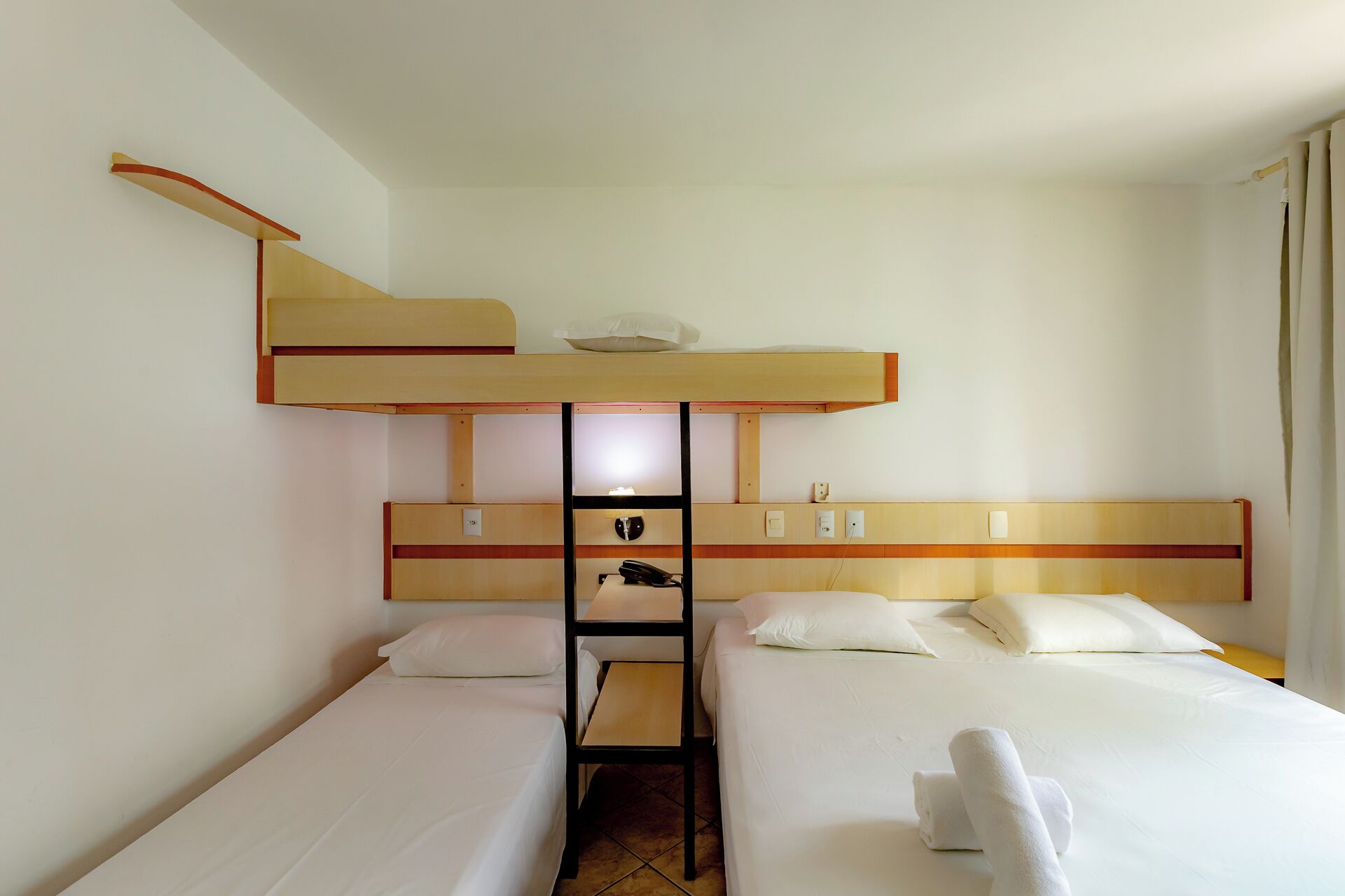 Ein Hotelzimmer mit zwei Einzelbetten, einem Schlafsofa und einem kleinen Schreibtisch sowie einem Telefon.