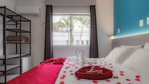 Habitación de hotel con cama, armario, ventana con cortinas y vista a palmeras.