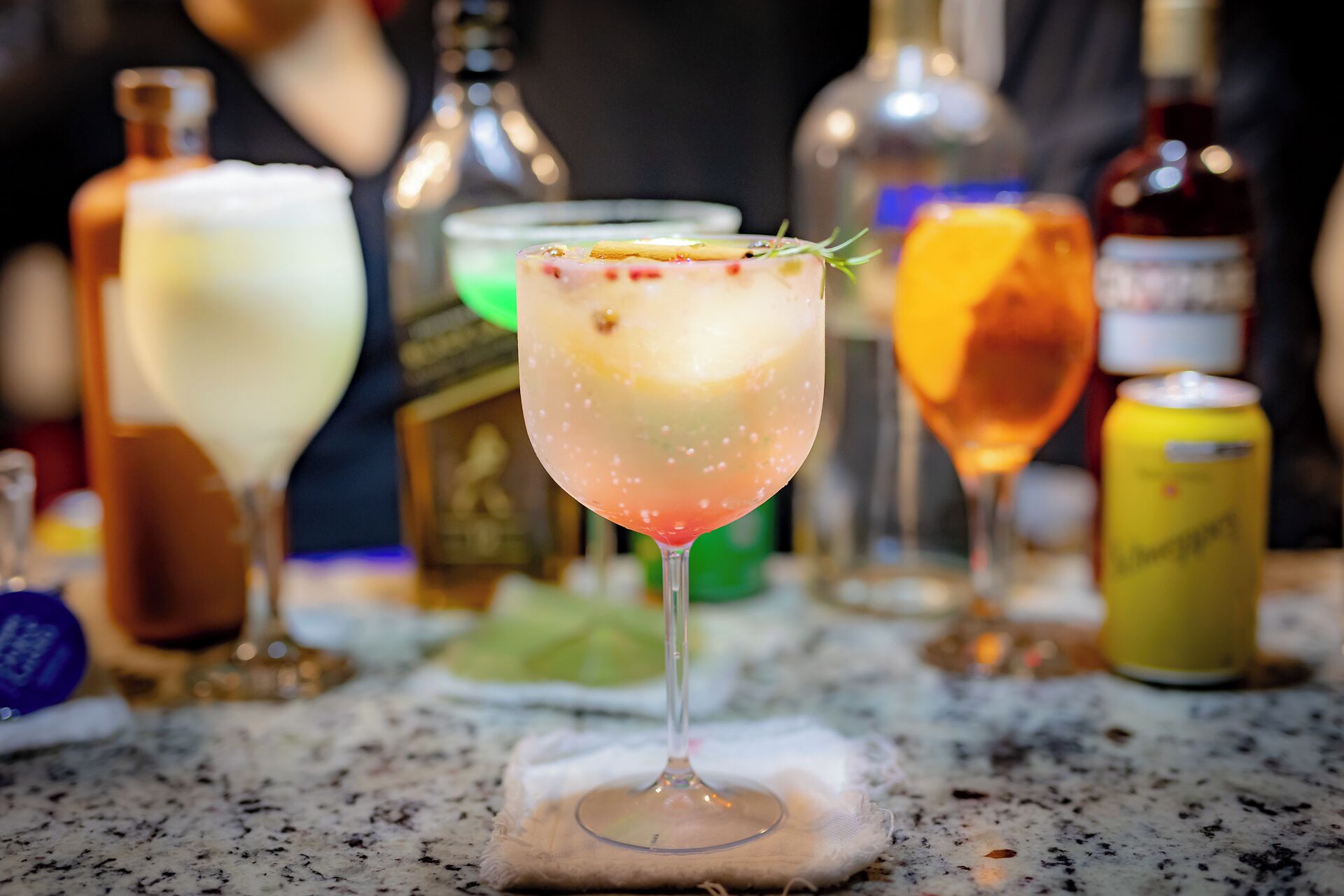 A bar setting with a cocktail glass in the foreground, surrounded by various bottles and a can.